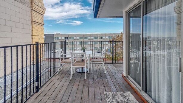 Een balkon met een tafel en stoelen, een leuning en uitzicht op een gebouw op de achtergrond.