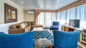 Een moderne woonkamer met een hoekbank, een blauwe fauteuil, een bijzettafeltje en een televisie.