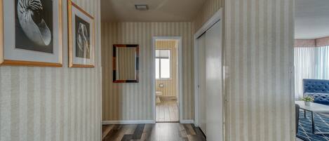 Um corredor com papel de parede listrado, quadros nas paredes, piso de madeira e vista para um banheiro.
