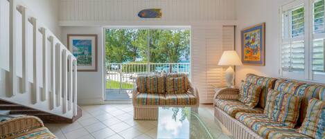 A spacious living area with a glass coffee table, wicker furniture, and a view of the outdoors.