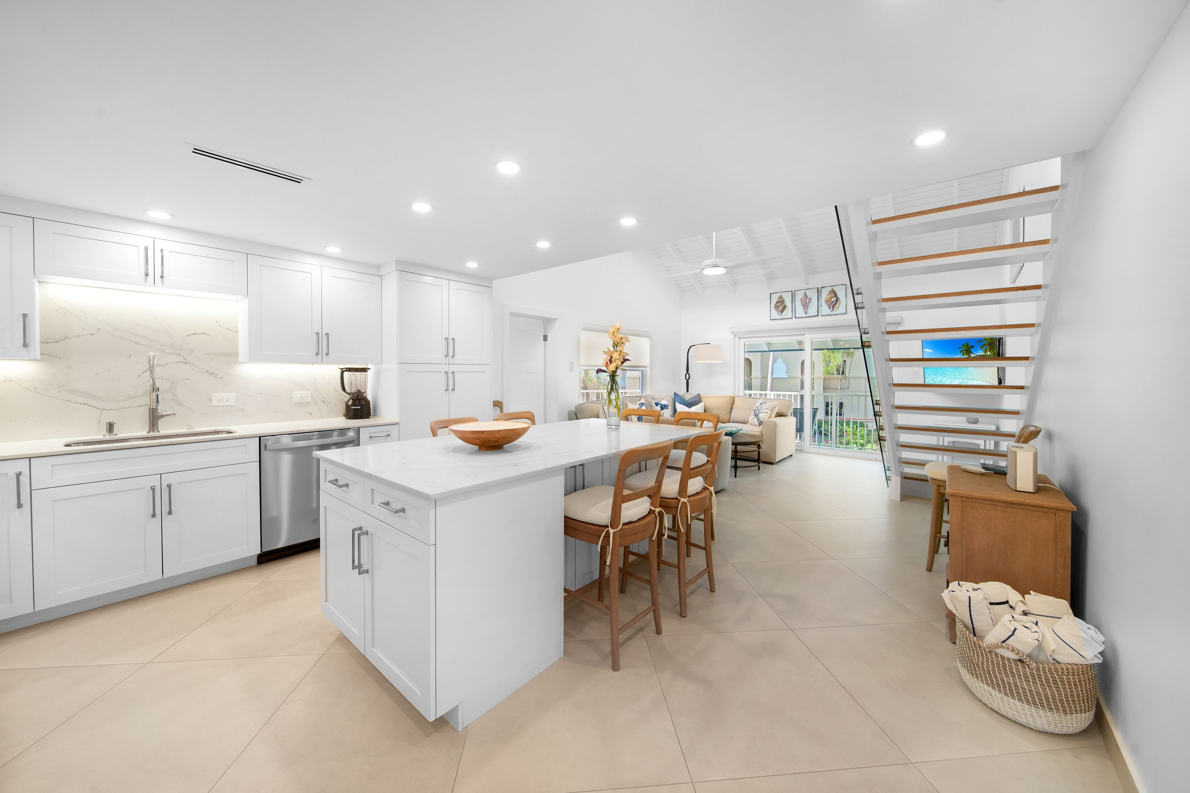 Une cuisine moderne avec des meubles blancs, un plan de travail en marbre et un îlot central doté de chaises.