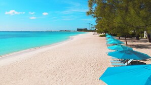 Une plage bordée d’une rangée de parasols bleus et de chaises longues le long du rivage.