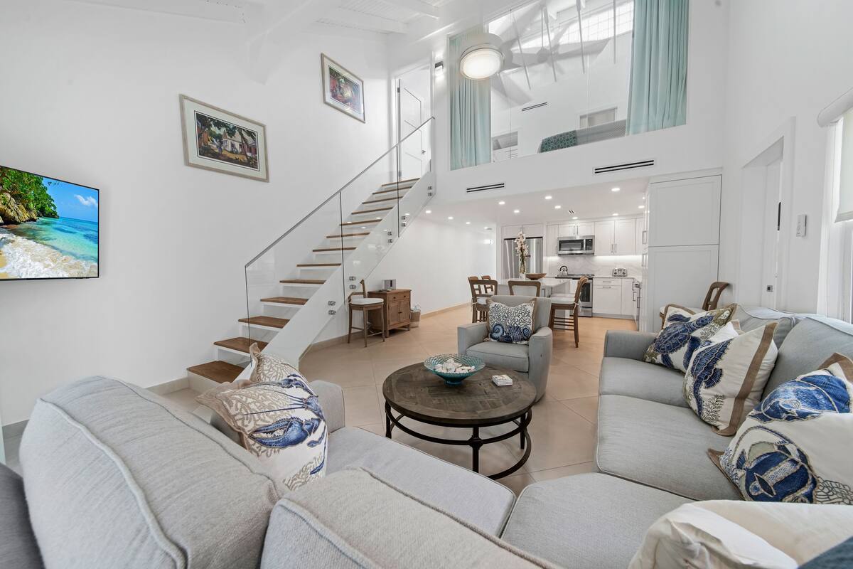 Un vaste espace de vie comprenant un canapé gris, une table basse et un escalier menant à un niveau supérieur.