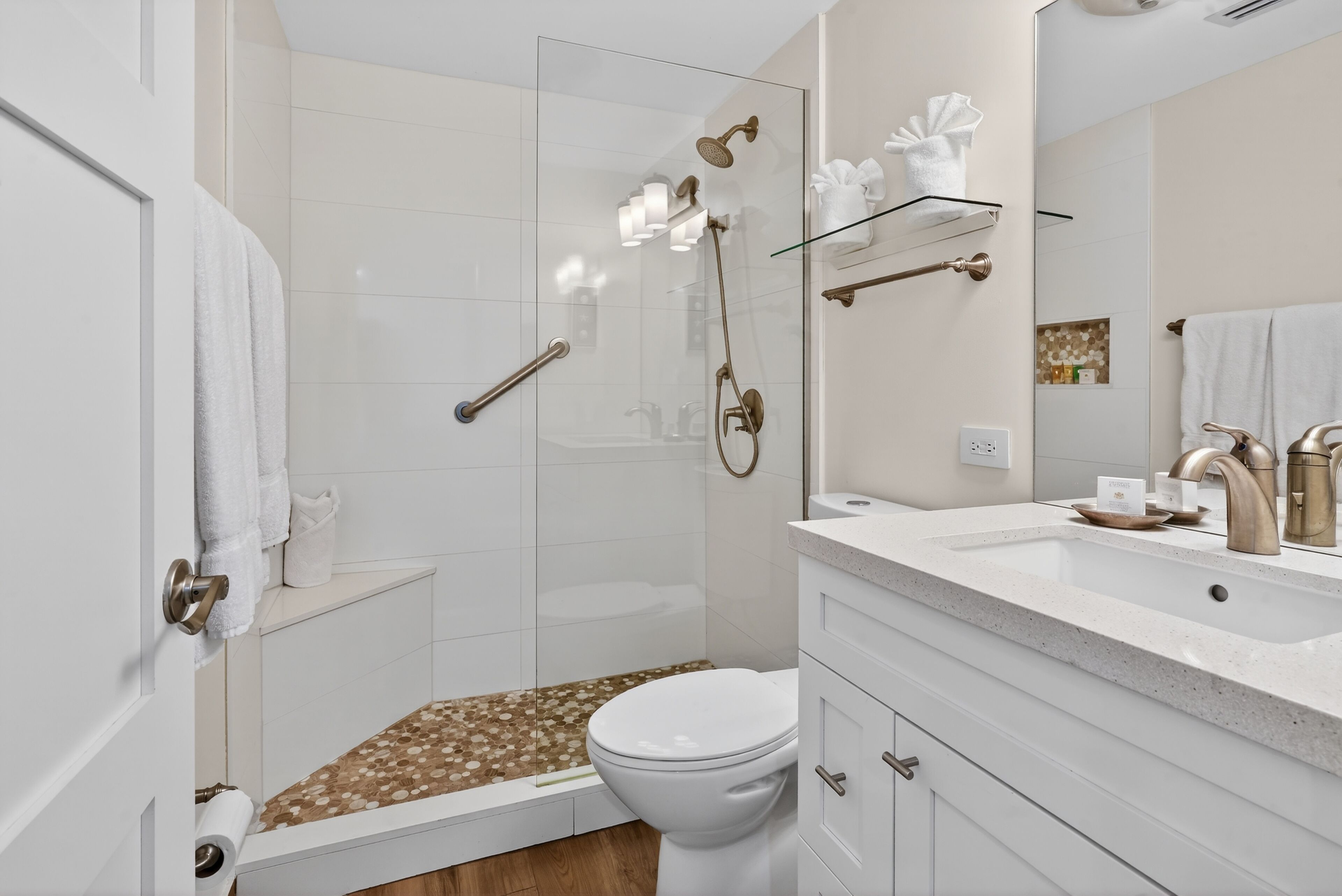 A modern bathroom with a glass shower enclosure, a white toilet, and a vanity with a sink and mirror.