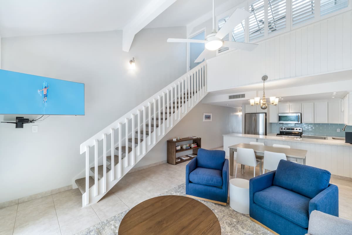Un vaste espace de vie comprenant un escalier, un canapé bleu, une table basse en bois et un coin cuisine équipé d’appareils électroménagers modernes.