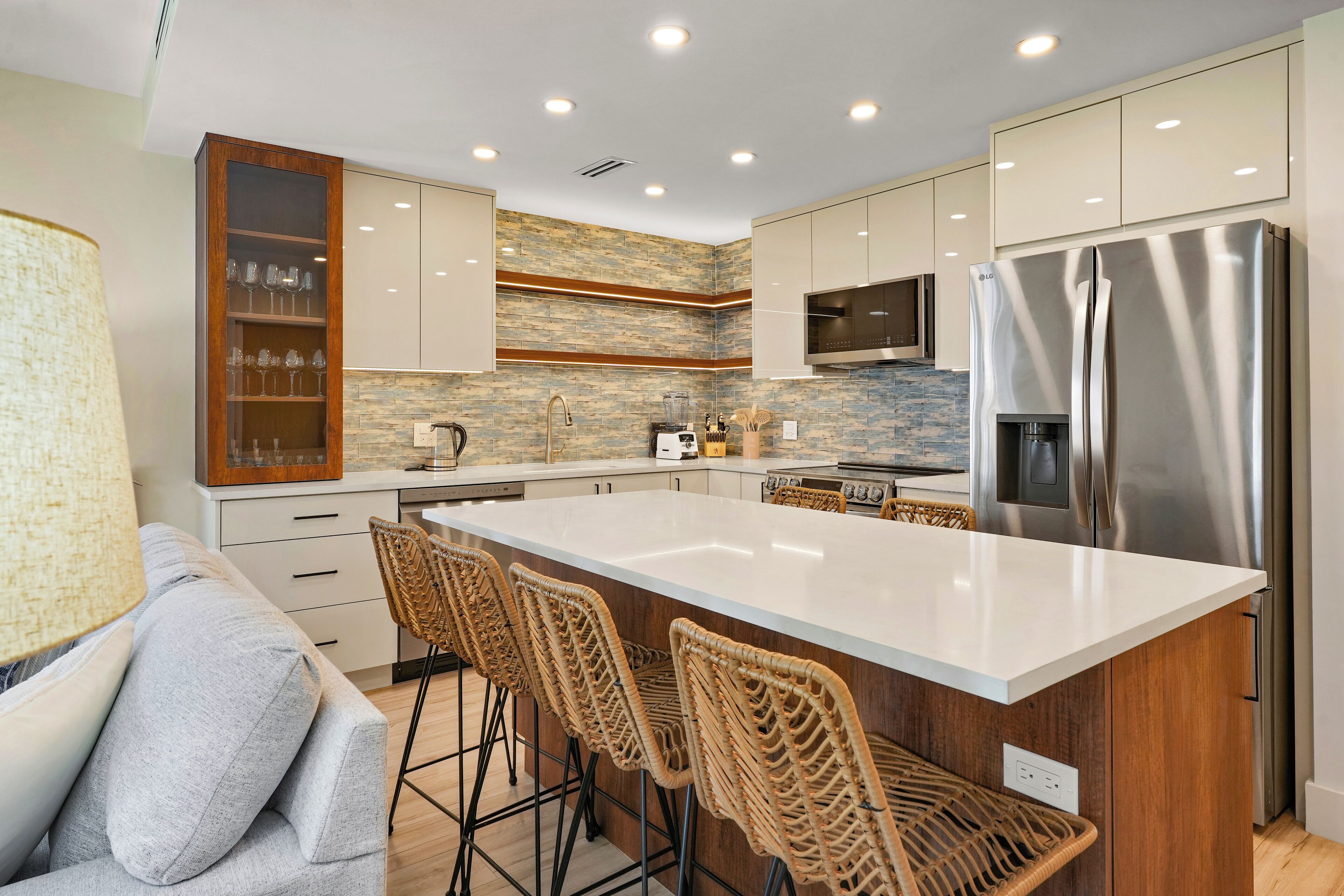 A modern kitchen with a large island, built-in appliances, and wicker bar stools.