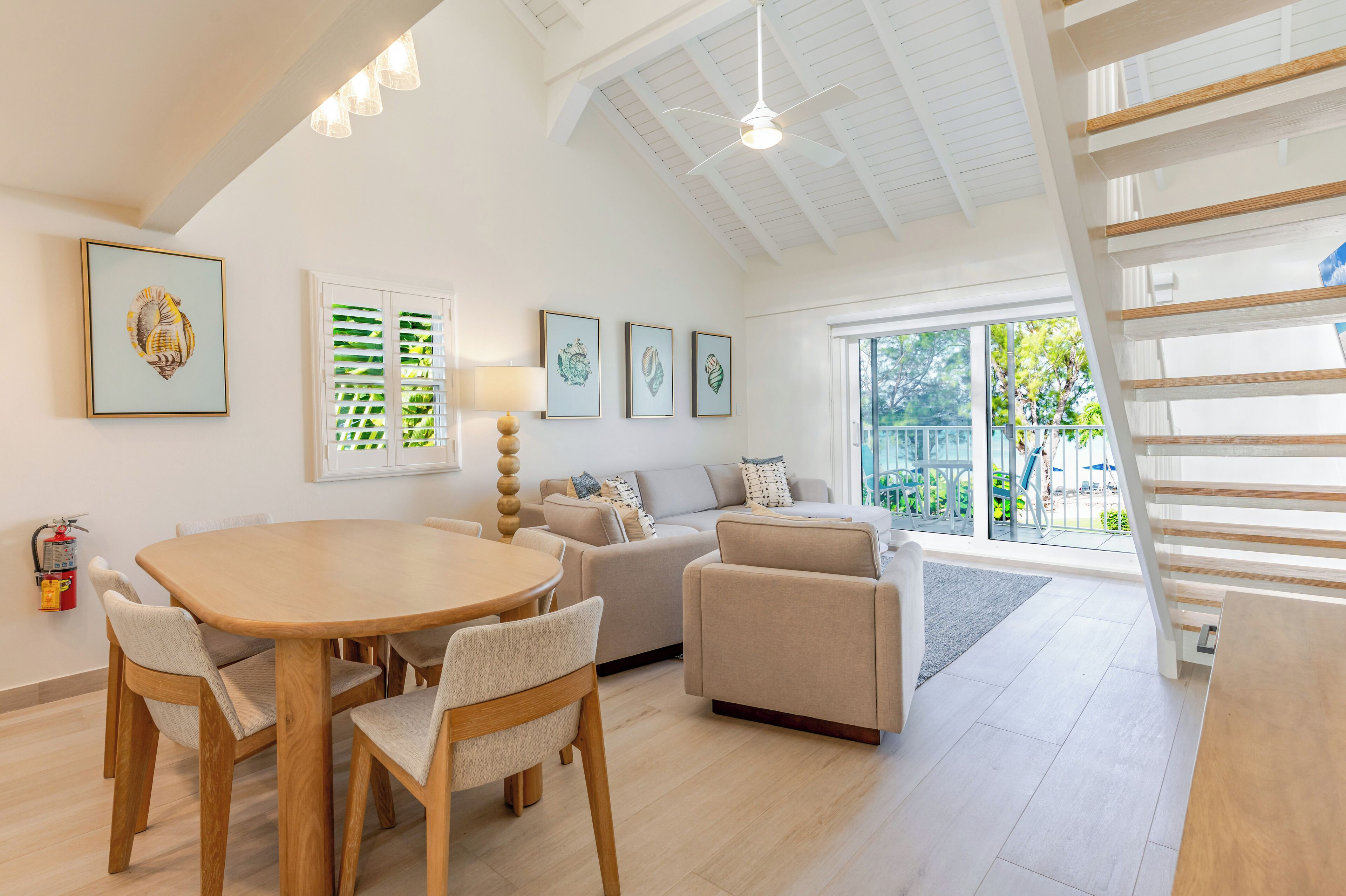 A spacious living area with a wooden dining table, beige sofas, and a staircase.