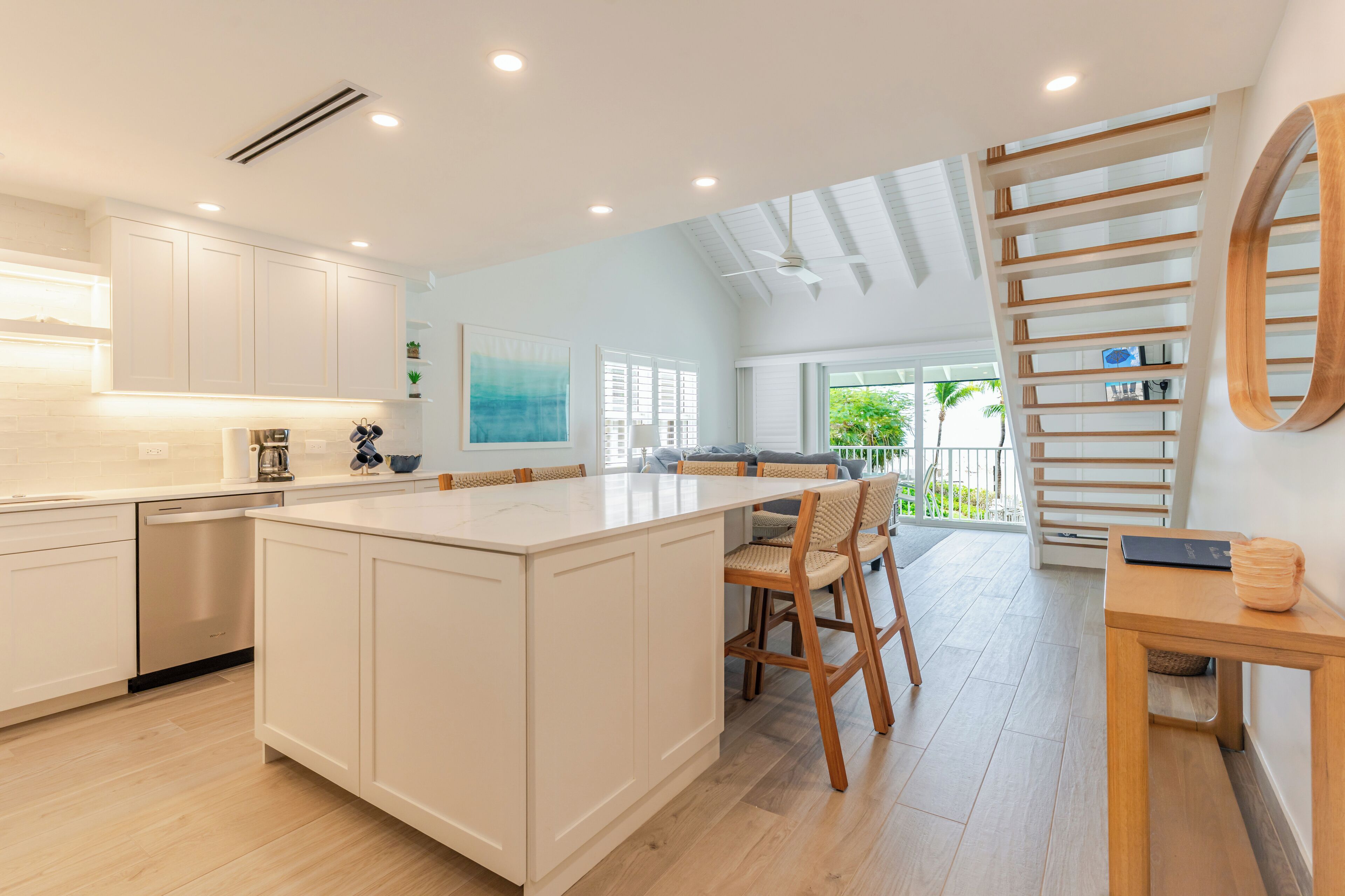 Une cuisine moderne avec des meubles blancs, un grand îlot central et un coin repas doté de chaises en bois.