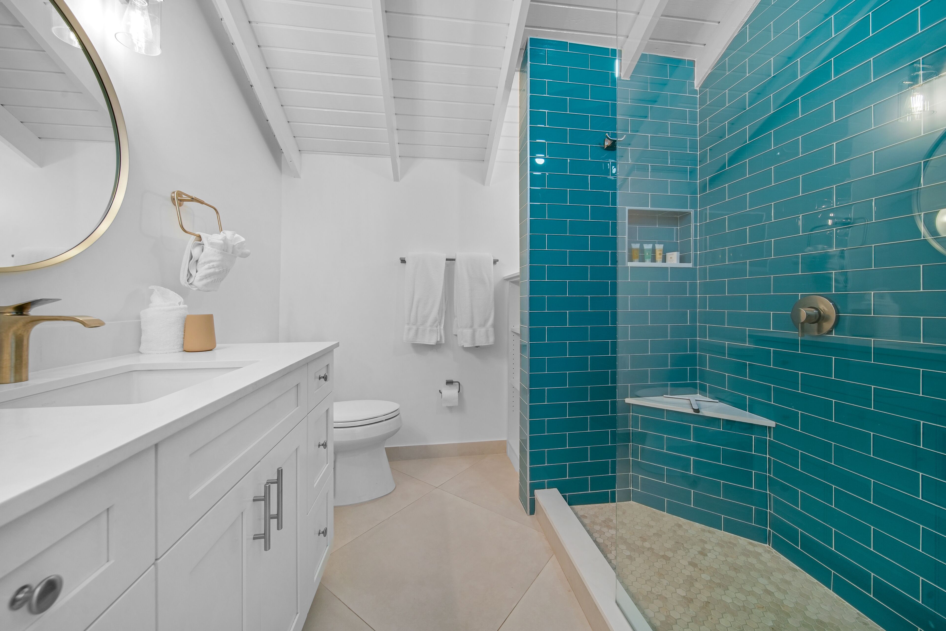A modern bathroom with a white vanity, a toilet, and a shower area with teal tiles.