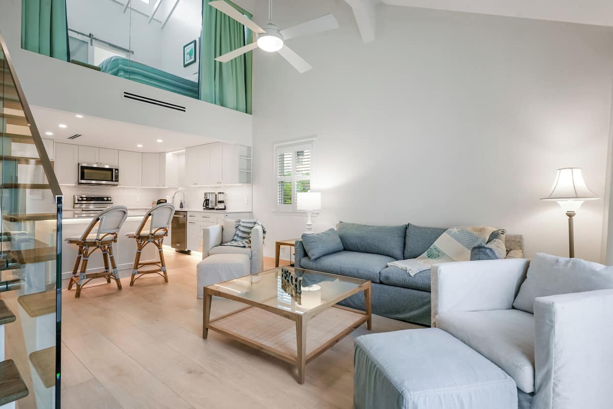 Un salon moderne avec une table basse en verre, un canapé et un coin repas avec des chaises en osier.