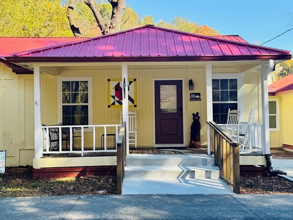 A yellow building with a purple roof, a front porch with white railings, and a wooden staircase leading to the door.