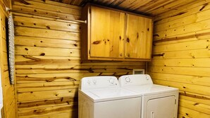 A laundry room with wooden walls and a double washer and dryer unit.