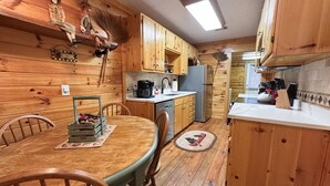 A wooden cabin-style kitchen with a dining table, chairs, and a refrigerator. - Downtown by Chattahoochee River, sit on front porch as horse and buggy stroll by (Helen)