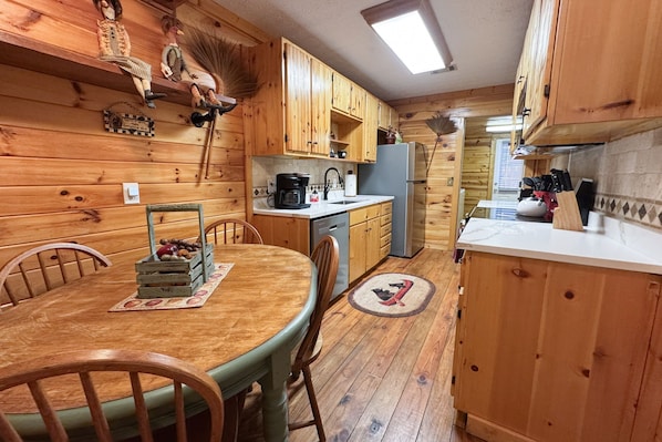 A wooden cabin-style kitchen with a dining table, chairs, and a refrigerator.