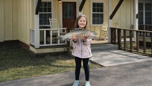 A person holding a fish in front of a house with a porch and a small deck. - Downtown by Chattahoochee River, sit on front porch as horse and buggy stroll by (Helen)