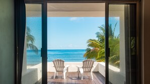 A balcony with two white chairs and a small table, overlooking a beach with palm trees and the ocean. - Beach house w/ private pool & sandy beach for 8 (San Miguel de Cozumel)