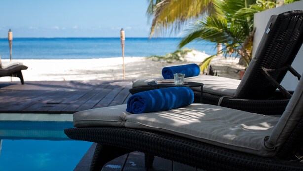 A poolside lounge chair with a cushion and a rolled towel, overlooking a beach and the ocean. - Beach house w/ private pool & sandy beach for 8 (San Miguel de Cozumel)
