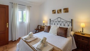 A hotel room with a bed, two bedside tables with lamps, a wooden chair, a window with curtains, and three wall art pieces.