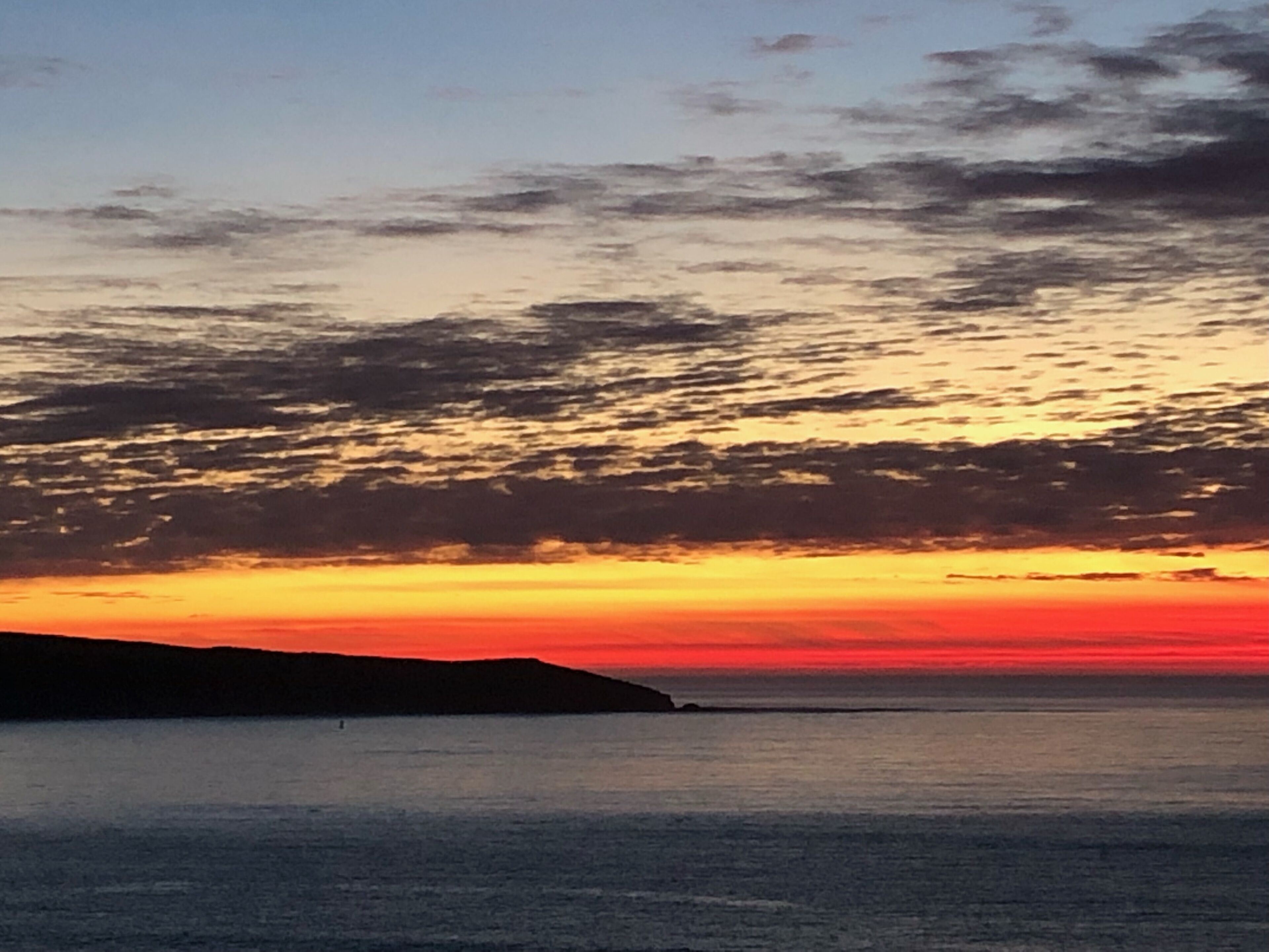 A sunset over a calm sea with a silhouette of a landmass in the distance.