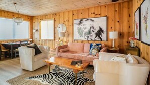 A cozy living room with a wooden interior, a large abstract painting, and a zebra rug. - Sundog Cottage - Clean & Cozy - EV - Walk to Food & Beach - Fenced Yard for Dog (Dillon Beach)