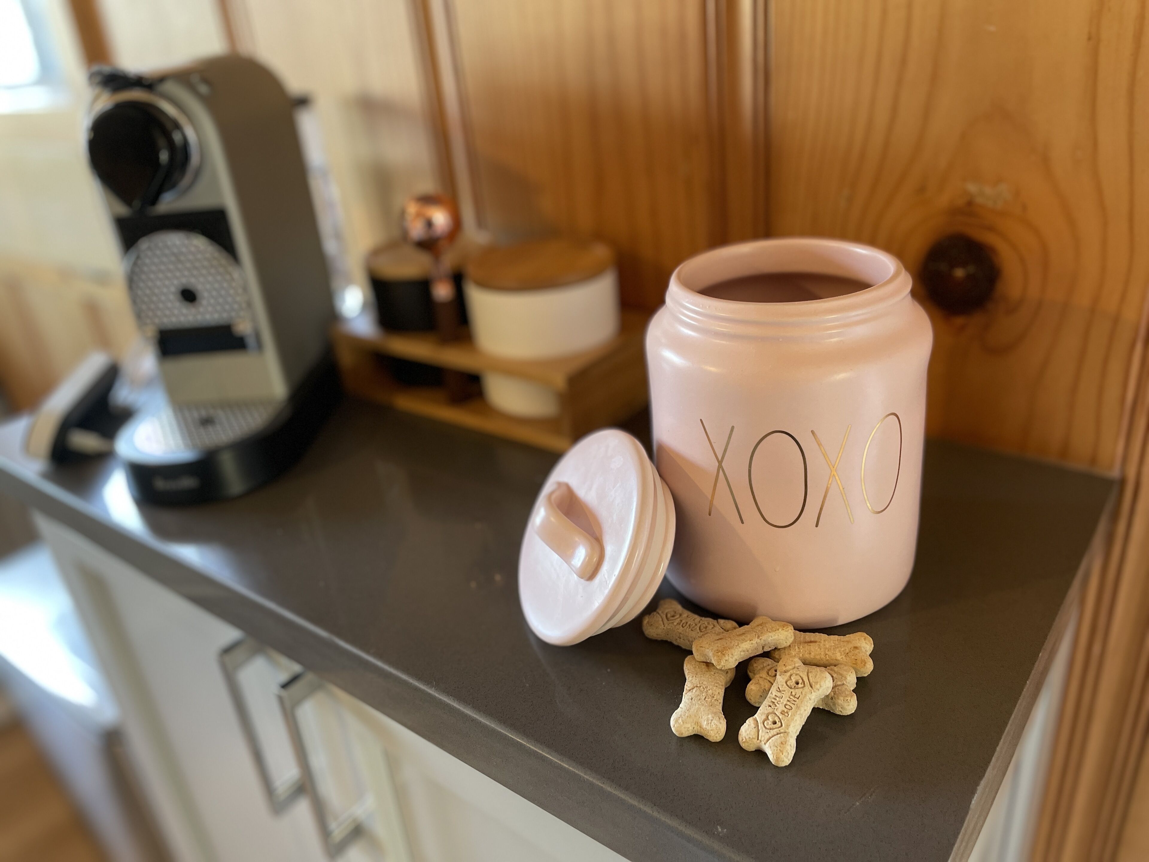A kitchen counter with a coffee maker, a pink container labeled "XOXO", and some dog treats.