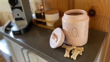 A kitchen counter with a coffee maker, a pink container labeled "XOXO", and some dog treats.