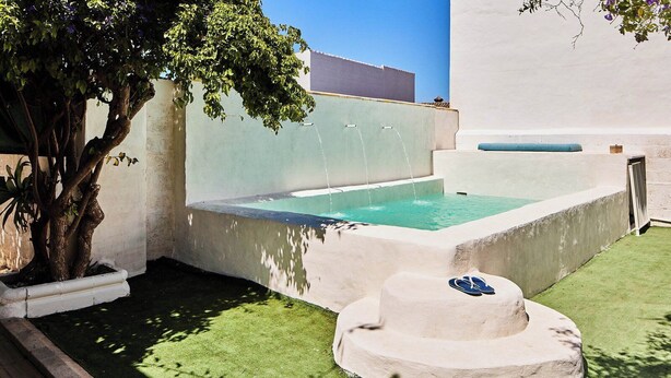 Une petite piscine extérieure, avec un arbre et un banc en pierre.