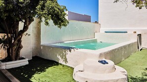 Una piccola piscina esterna con un albero e una panchina in pietra.