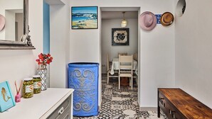 Un couloir avec un mur blanc, un baril décoratif bleu, un coin repas avec une table et des chaises, et un tableau encadré accroché au mur.