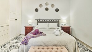 Une chambre à coucher bien aménagée, avec un lit, deux tables de chevet, une commode, un tapis à motifs et des œuvres d’art décoratives accrochées au mur.