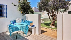 Une terrasse avec une table ronde, des coussins bleus et un arbre en pot.