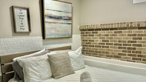A neatly made bed with a quilted bedspread, a pillow, and rolled towels. There is a framed quote on the wall and a painting above the bed. - Charming 2 Bedroom Apt. Close to Valparaiso University Short-Term Stays (Valparaiso)