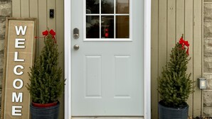 A white door with a window, flanked by two potted Christmas trees, and a 'WELCOME' sign. - Charming 2 Bedroom Apt. Close to Valparaiso University Short-Term Stays (Valparaiso)
