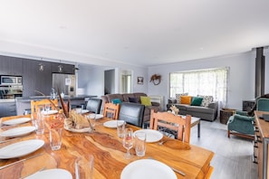 A modern living room with a dining area, grey sofas, and a kitchen in the background.
