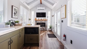 A modern kitchen with a stone fireplace, wooden ceiling beams, and a large window with blinds. - Near Zion • Modern Tiny Home • Hiking & MTB Access (Apple Valley)