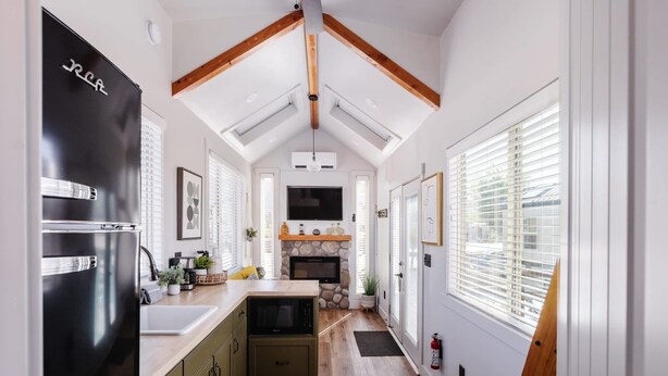 A modern kitchen with a black refrigerator, wooden beams, a stone fireplace, and a large TV. - Near Zion • Modern Tiny Home • Hiking & MTB Access (Apple Valley)