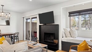 A modern living room with a fireplace, a flat-screen TV, a sofa, and a dining area. - Outpost: Cedars 1413 - Aspens Location! (Wilson)