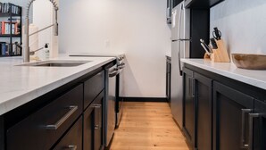 A modern kitchen with dark cabinetry, a wooden floor, and a stainless steel sink. - Outpost: Cedars 1413 - Aspens Location! (Wilson)