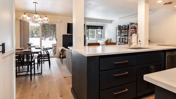 A modern kitchen with a large island, black cabinetry, and a dining area with a table and chairs. - Outpost: Cedars 1413 - Aspens Location! (Wilson)