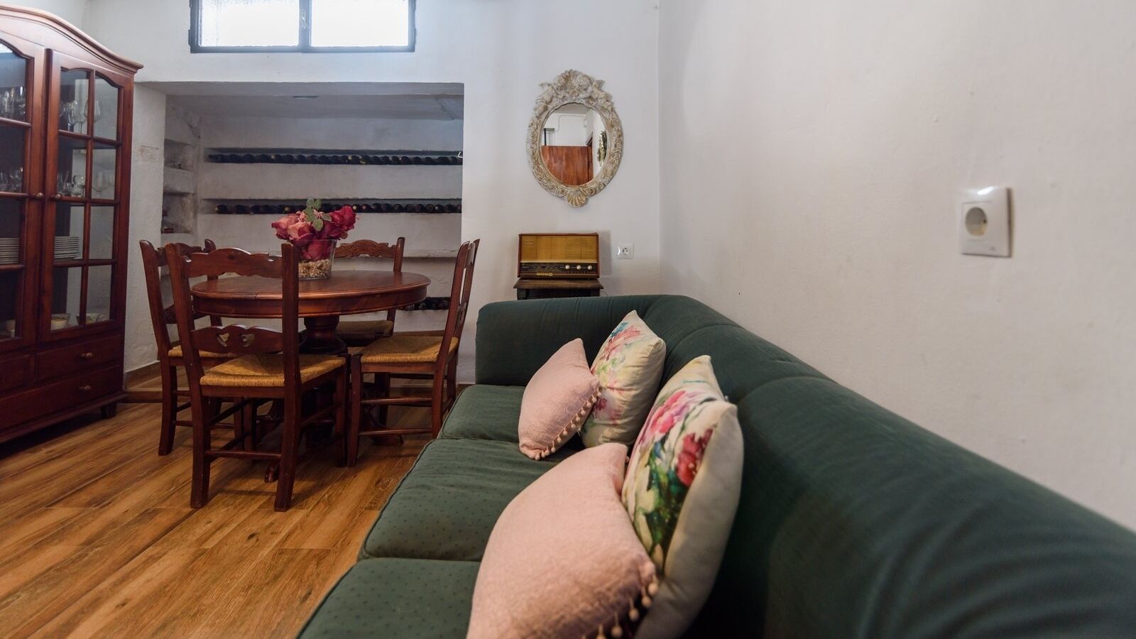 A living room with a green sofa, wooden dining table, chairs, and a cabinet.