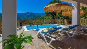 A pool area with lounge chairs and a thatched umbrella, surrounded by a wooden fence and greenery. - Casa Rural Monte Dios Jubrique by Ruralidays (Málaga)