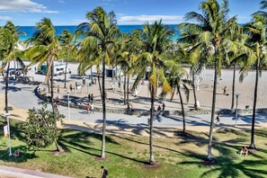 A beachside area with palm trees, a paved walkway, and a view of the ocean. - Amazing 4BR direct oceanfront PH by YouRent! (Miami Beach)