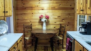 A wooden-paneled kitchen with a wooden table and chairs, a vase with flowers, and a coffee machine.