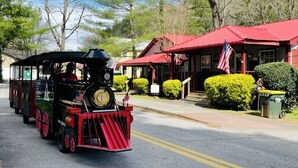 Un petit train avec une locomotive noire et des wagons rouges, passant devant un bâtiment doté d’un toit rouge et arborant un drapeau américain.