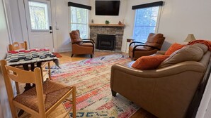 Un salon avec une cheminée, deux fauteuils en cuir, un canapé, une table basse sur laquelle est posé un jeu de société et un tapis à motifs.