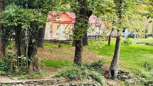 Un cadre paisible au bord de la rivière, avec un mur de pierre, une végétation luxuriante et, au loin, un bâtiment surmonté d’un toit rouge.