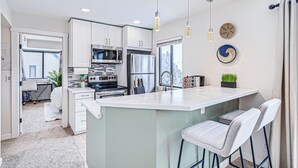 A modern kitchen with white cabinets, a central island, bar stools, and pendant lighting.