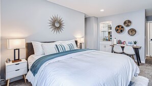 A modern bedroom with a large bed, bedside tables, a mirror, and wall decor.