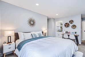 A modern bedroom with a large bed, bedside tables, a mirror, and wall decor.