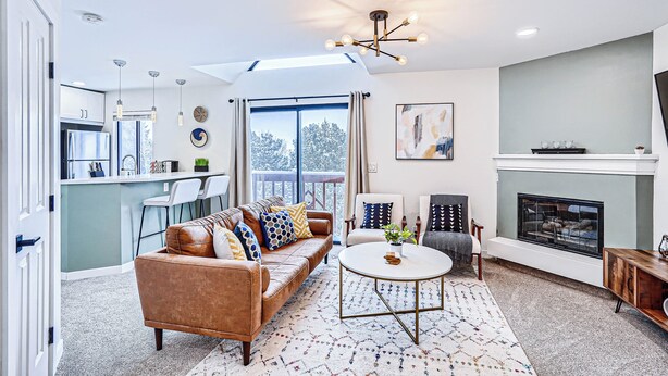 A modern living room with a sofa, chairs, a fireplace, and a kitchen in the background.